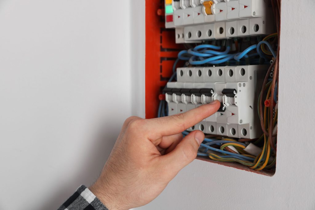 A hand switching a breaker in an open household panel