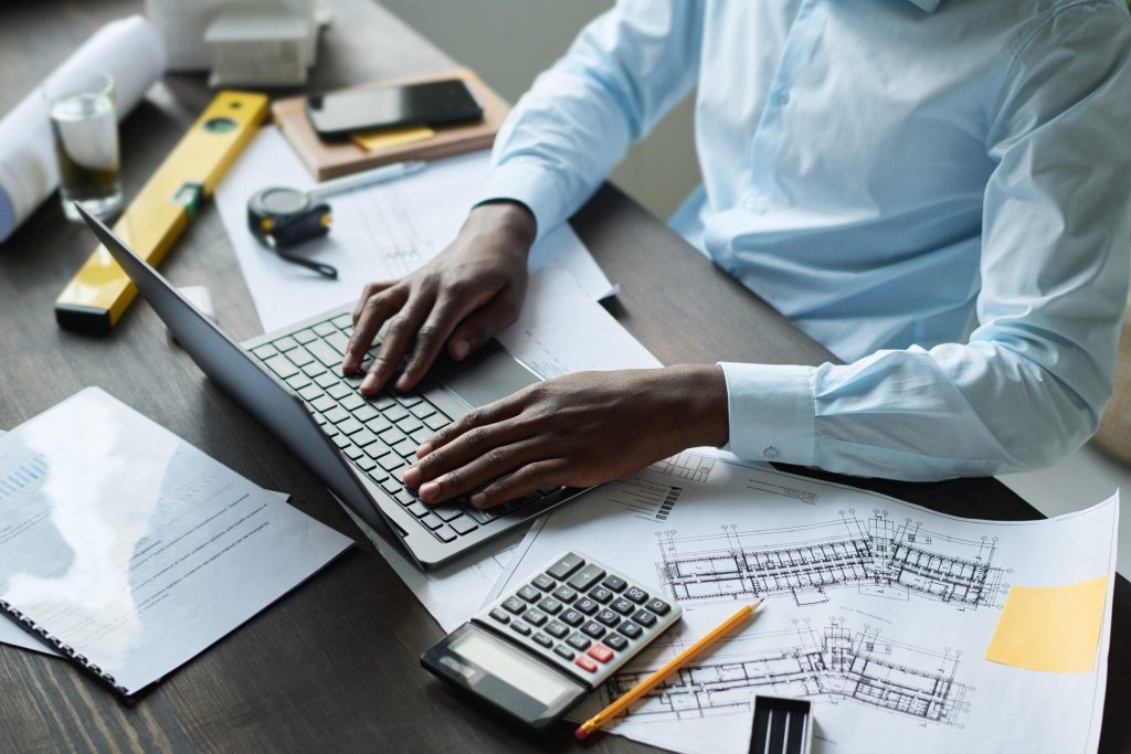 Hands at a laptop on a desk with a calculator, a tape measure, a spirit level and drawings