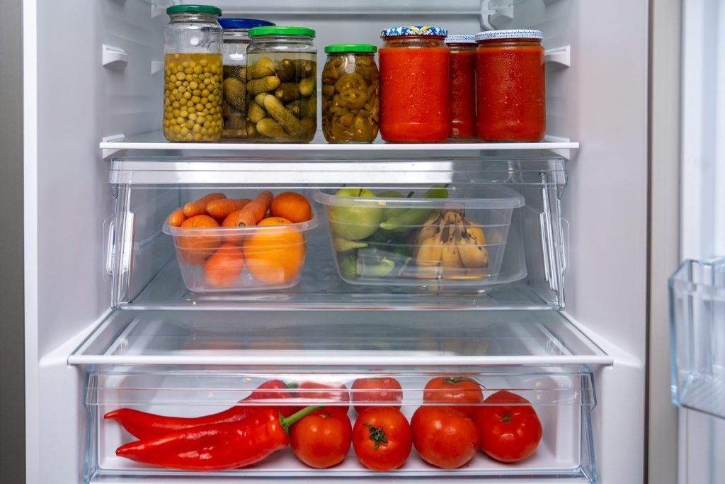 An open refrigerator packed with jars, containers of fruit and vegetables in the crisper