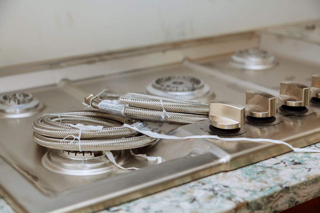 A cooktop with its grates lifted off, burner heads and gas lines exposed