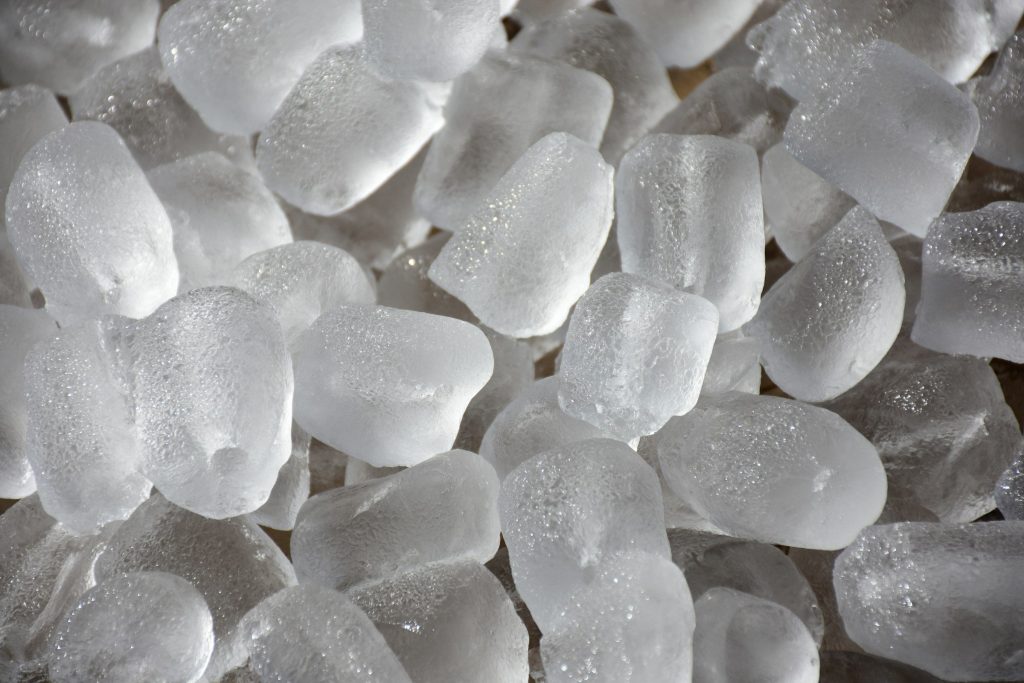 A close heap of machine-made ice cubes, hollow-ended, wet at the edges