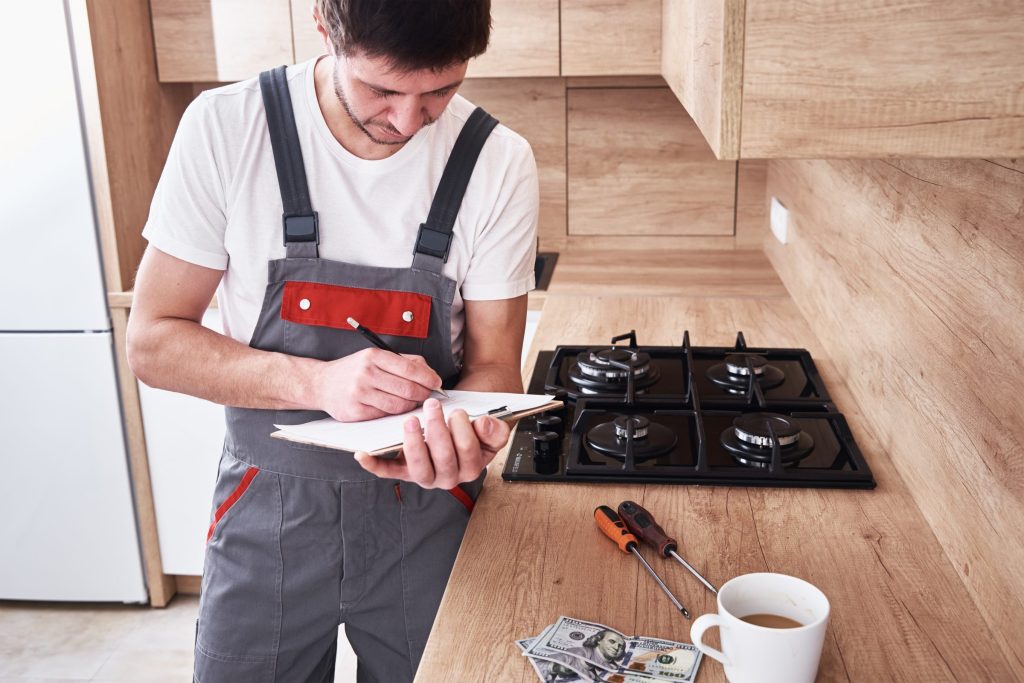 A technician writing on a clipboard beside a gas cooktop