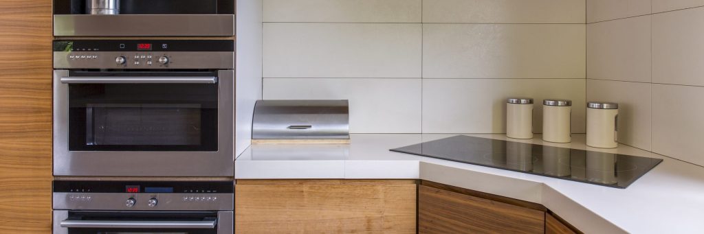 A stainless microwave and oven stacked in a wood run, displays lit red