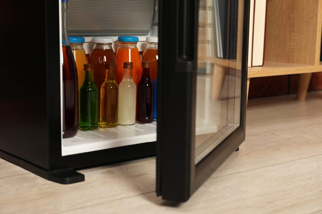 A glass-fronted undercounter beverage center stocked with bottles, its door ajar