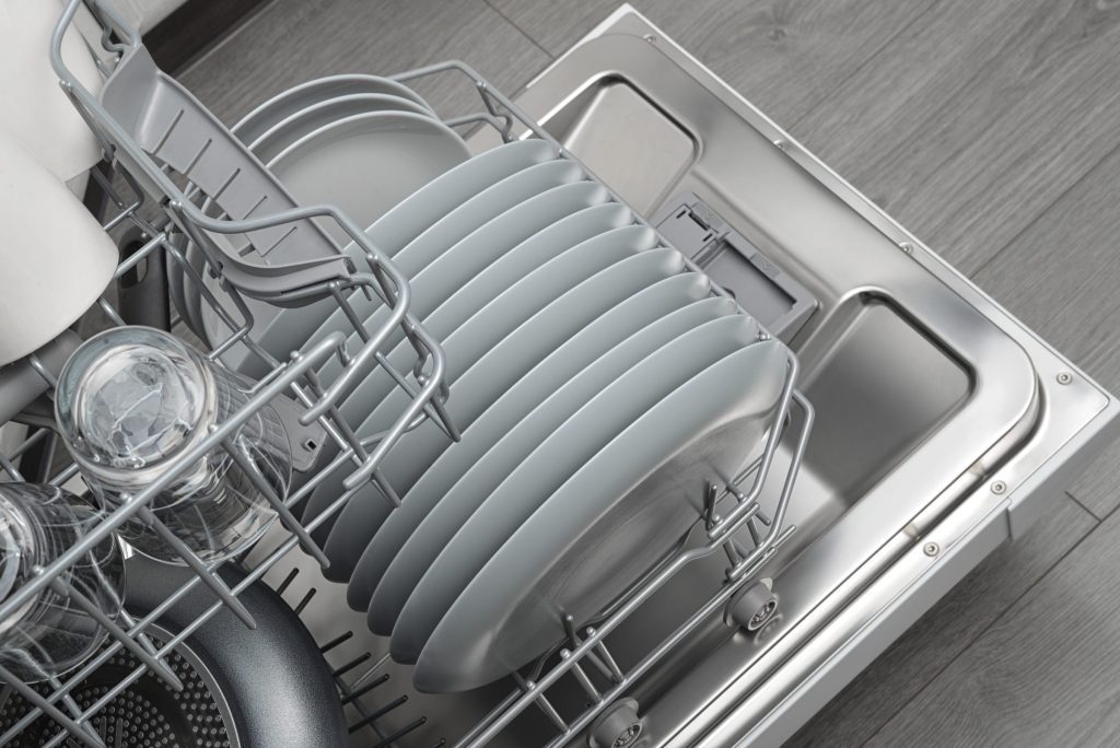 Looking down into an open dishwasher — grey plates on end in the lower rack, glasses at the left, the door's inner face at the right