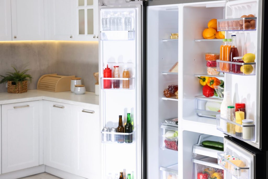 A side-by-side refrigerator with both doors open in a white kitchen, shelves full of food