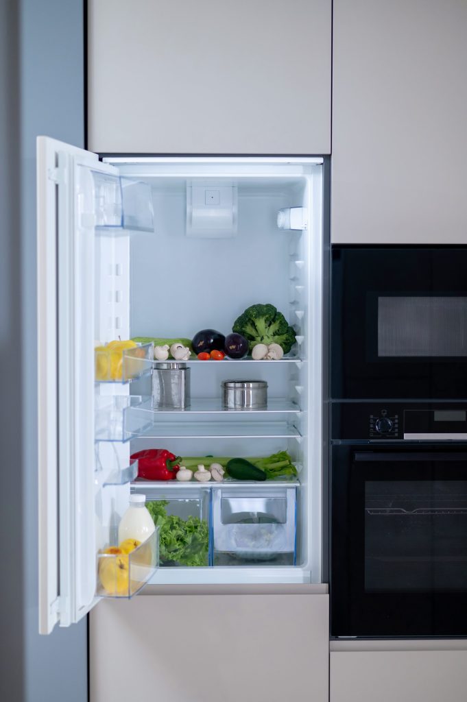 A built-in refrigerator standing open in a run of pale cabinetry, a microwave and an oven column at the right