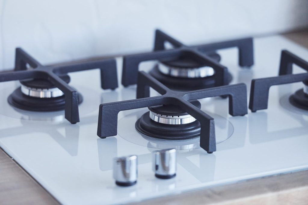 A white glass gas hob with cast grates, from above