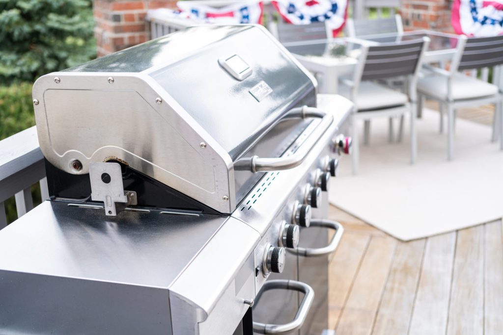 A stainless gas grill with the lid raised on a timber deck