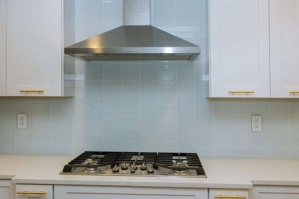 A stainless hood over a gas cooktop in a white tiled kitchen
