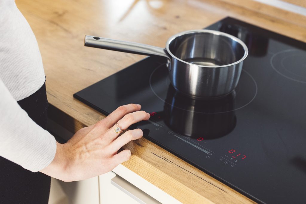 A hand at the slider of an induction hob set in an oak worktop, a steel saucepan on the ring
