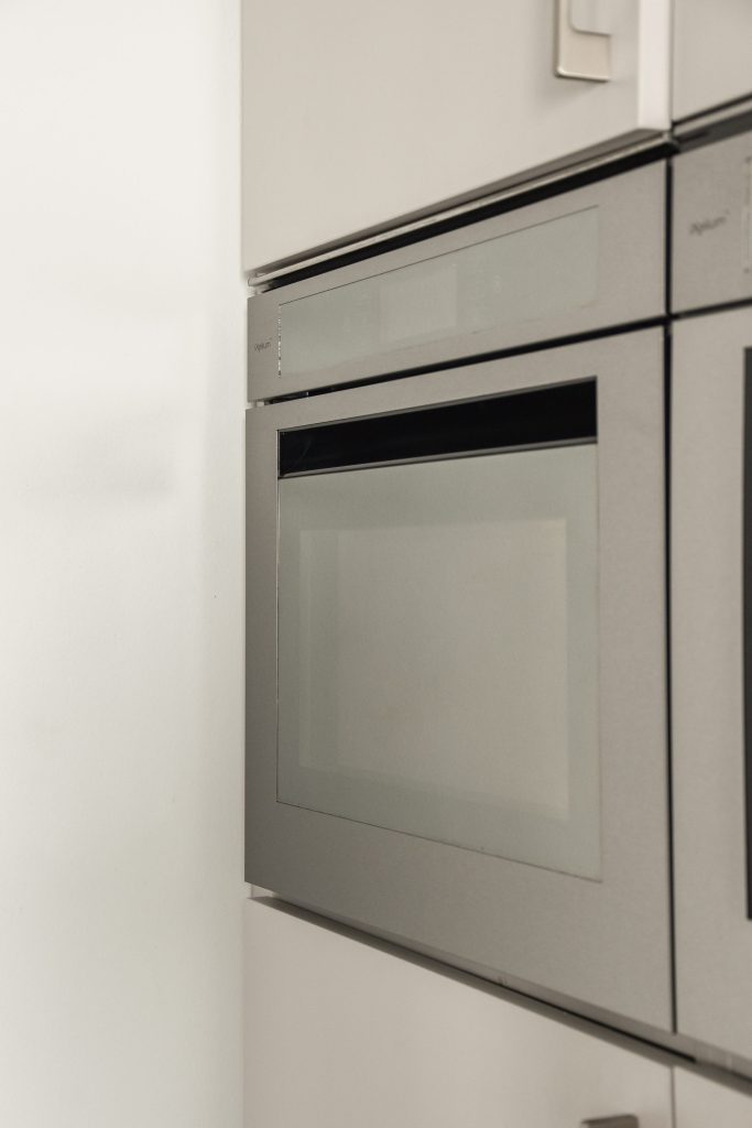 A slim built-in oven in a white cabinet run. Front zoomed at 3x: cabinet joints, no lettering