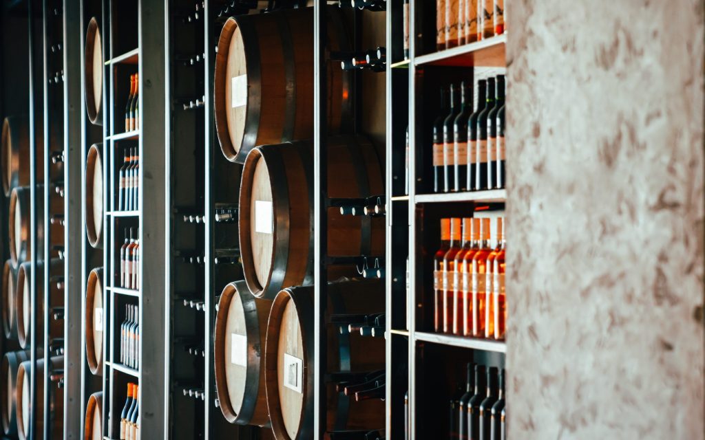 A lit wine room with barrels and bottles ranged along the shelves