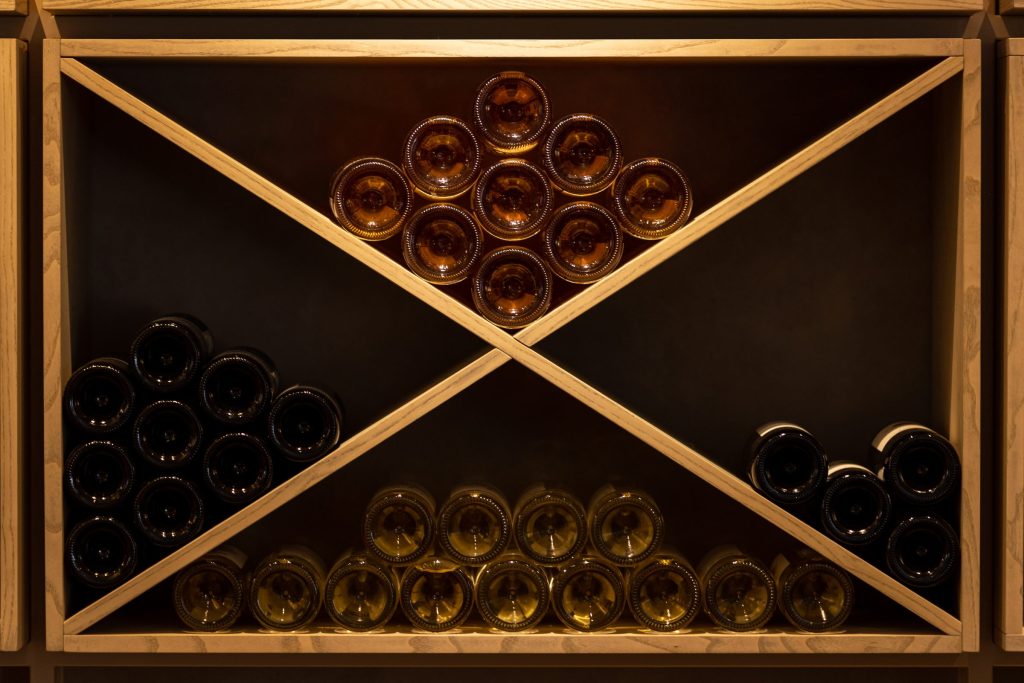 Bottles stacked in a wooden X-frame rack under warm light