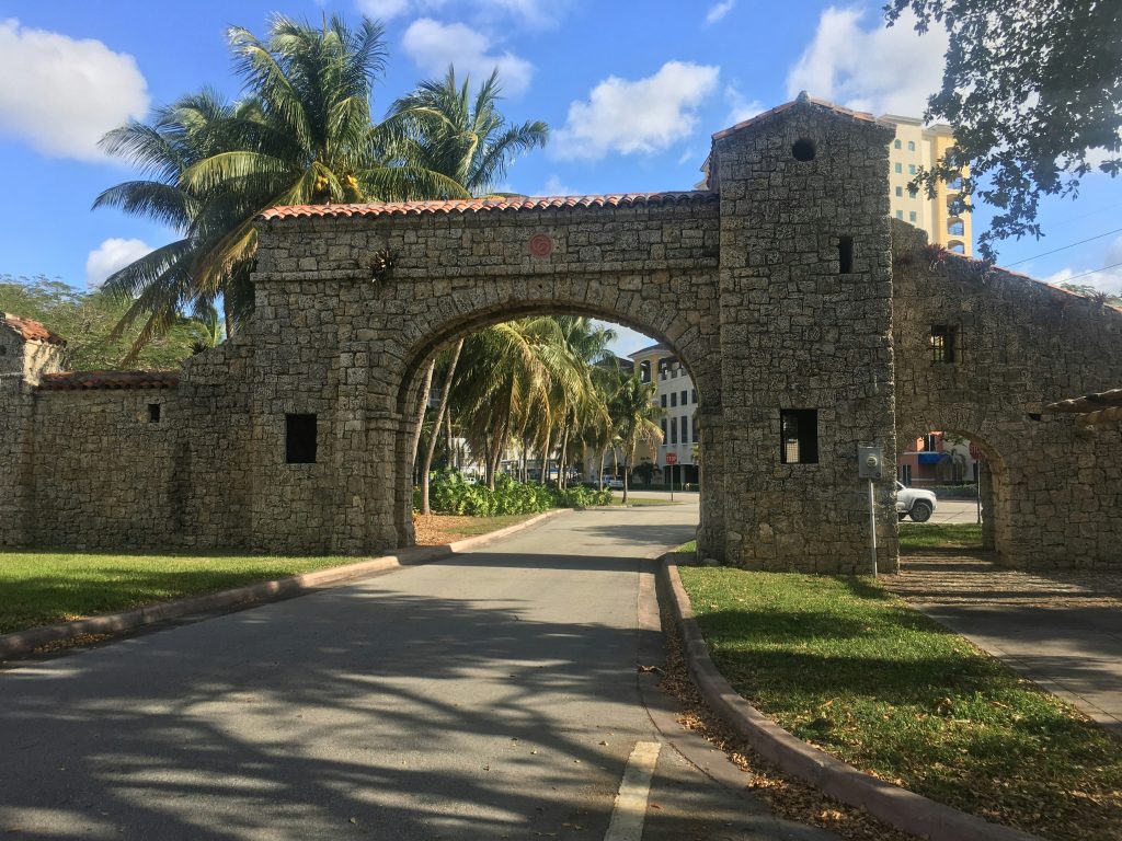 A coral-rock entrance arch across a road lined with palms