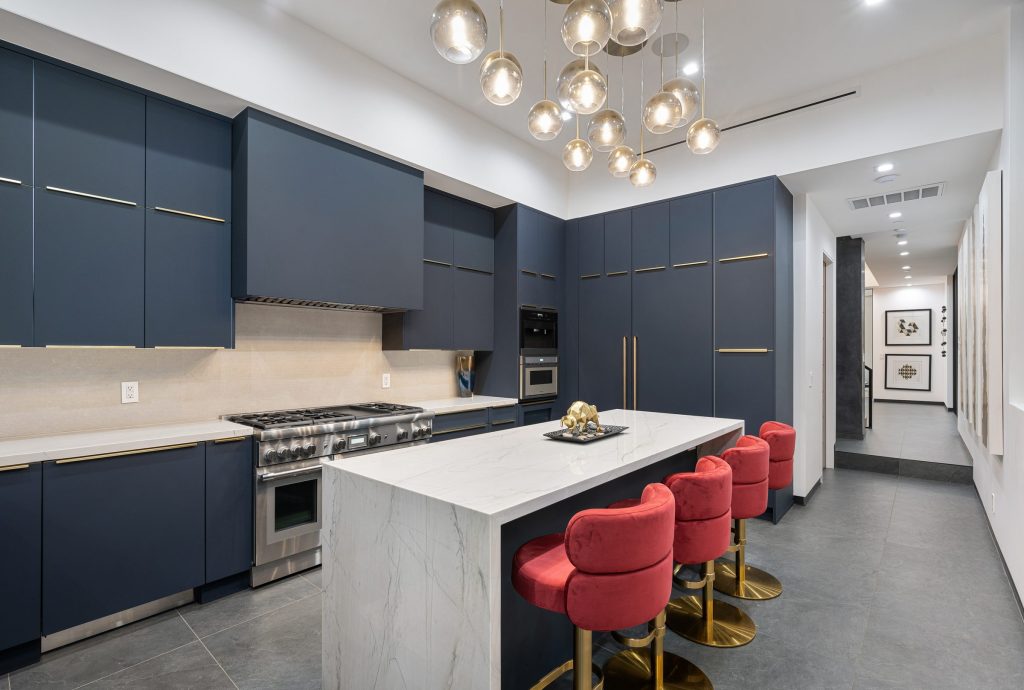 A professional gas range with a griddle set into a navy kitchen run beside a marble island