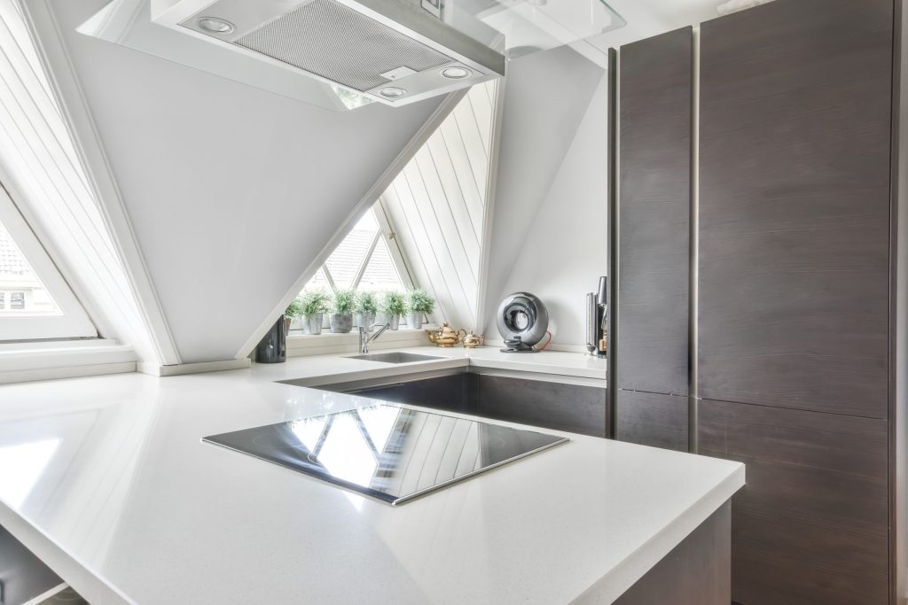 An induction hob in a white stone worktop with a tall dark appliance column standing beside it