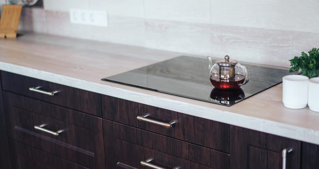 A glass teapot on a black hob set into a dark wood run