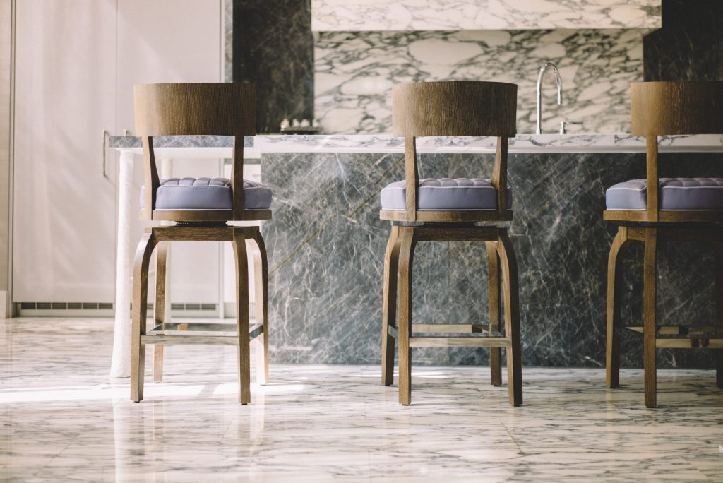 Bar stools drawn up to a marble island run in a pale kitchen