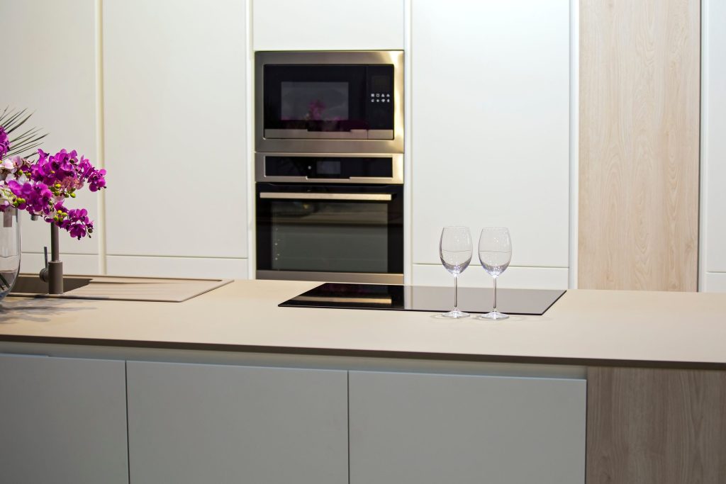 A pale minimal kitchen with an induction hob set into the island and a built-in oven column behind it