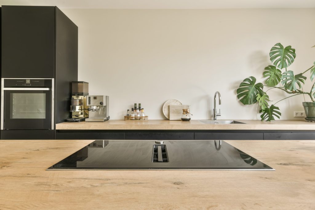 An oak island with a black hob set into it, a wall oven column behind