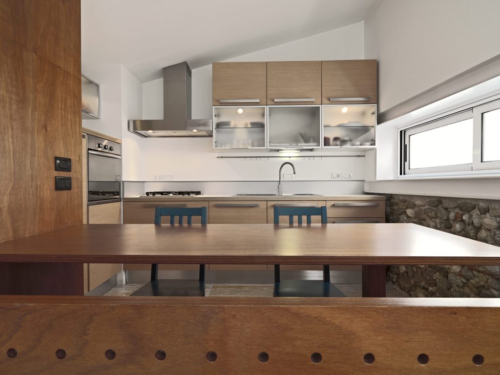 A pale wood kitchen with a stainless chimney hood and a long table