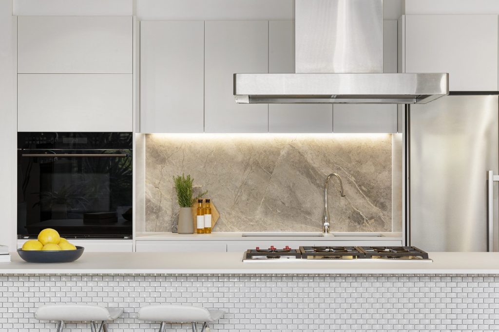 A gas rangetop set into a stone-topped island under a stainless island hood, a tall refrigeration column beside it