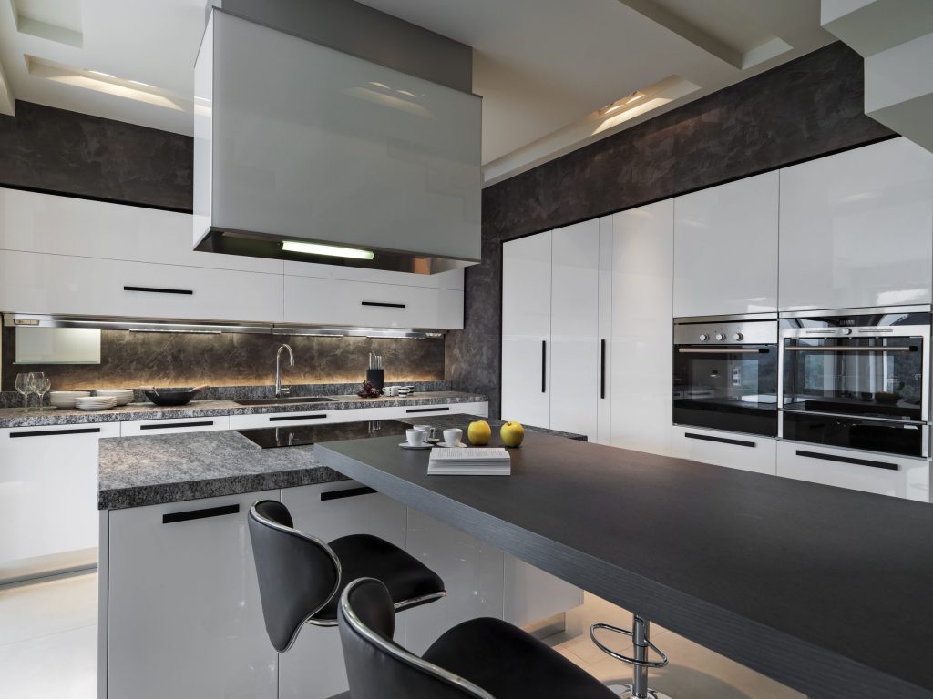 A white gloss kitchen with two built-in wall ovens and a long stone-topped island