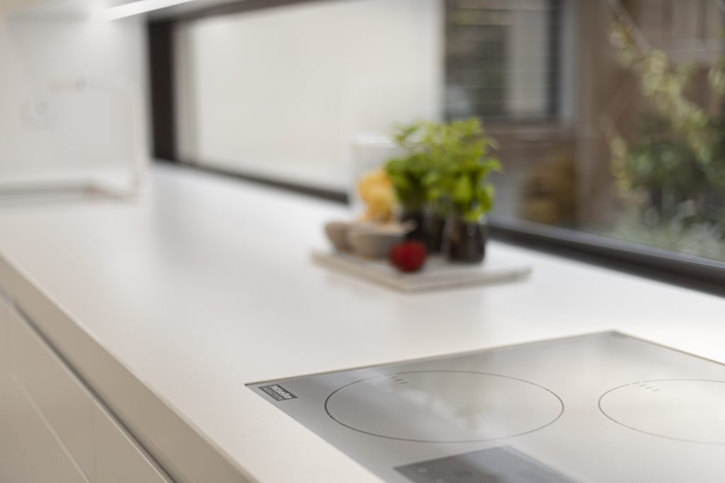 A white counter with an induction hob under a long window