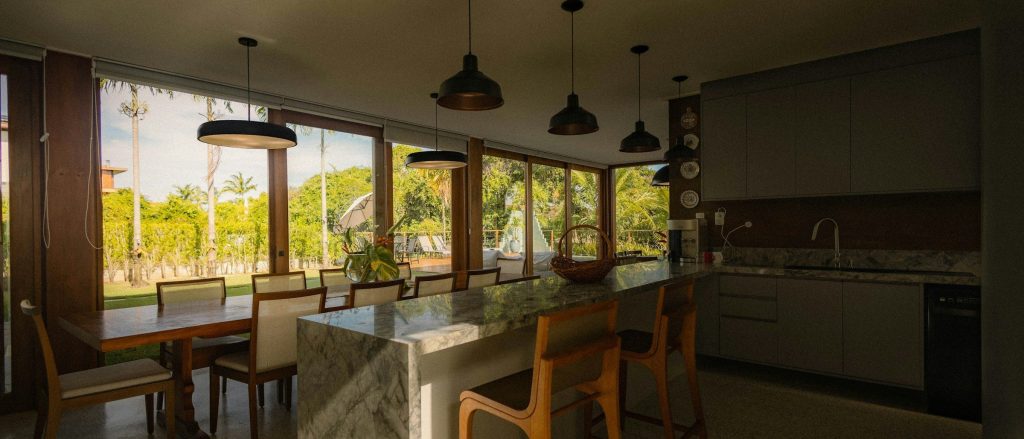 A dark kitchen and dining table looking out on palms through a long window