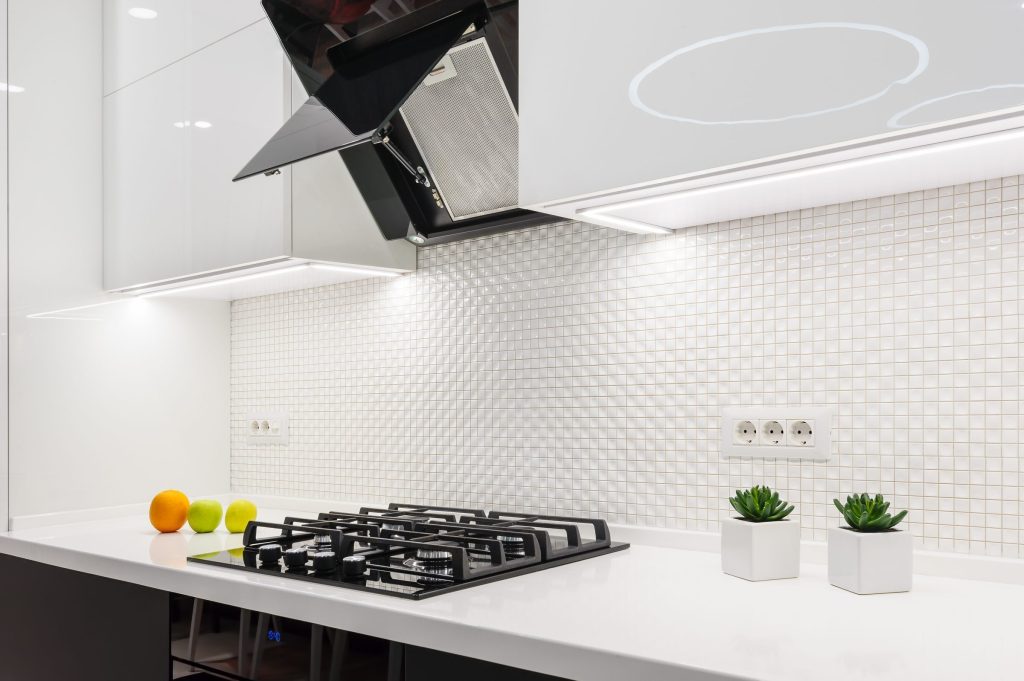 A white kitchen with a mosaic splashback, angled hood and gas cooktop