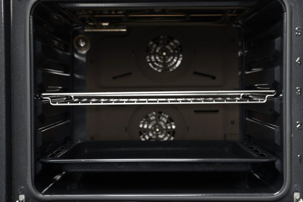 The empty black cavity of an oven with two fan covers on the back wall