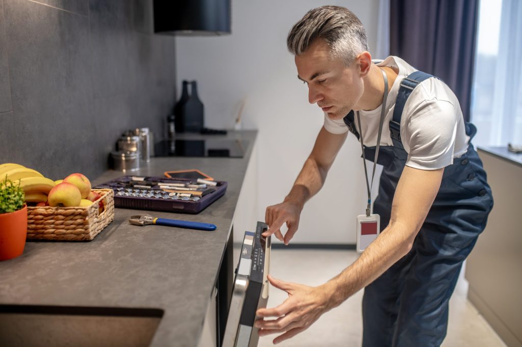 A technician reading a cooktop control panel with a socket set open on the counter beside him