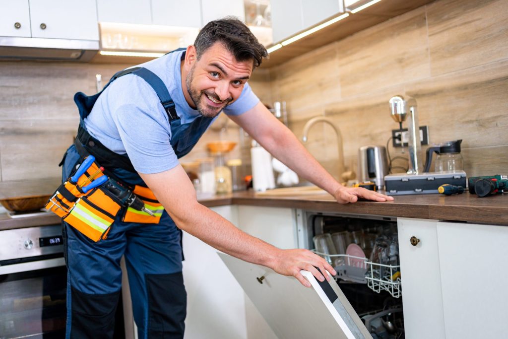 A technician opening a loaded dishwasher door under a wooden worktop