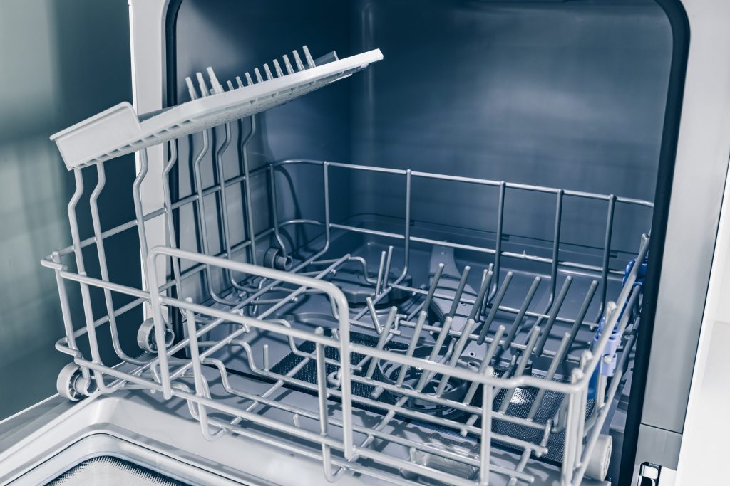 The empty racks and floor of a dishwasher tub with the door lowered