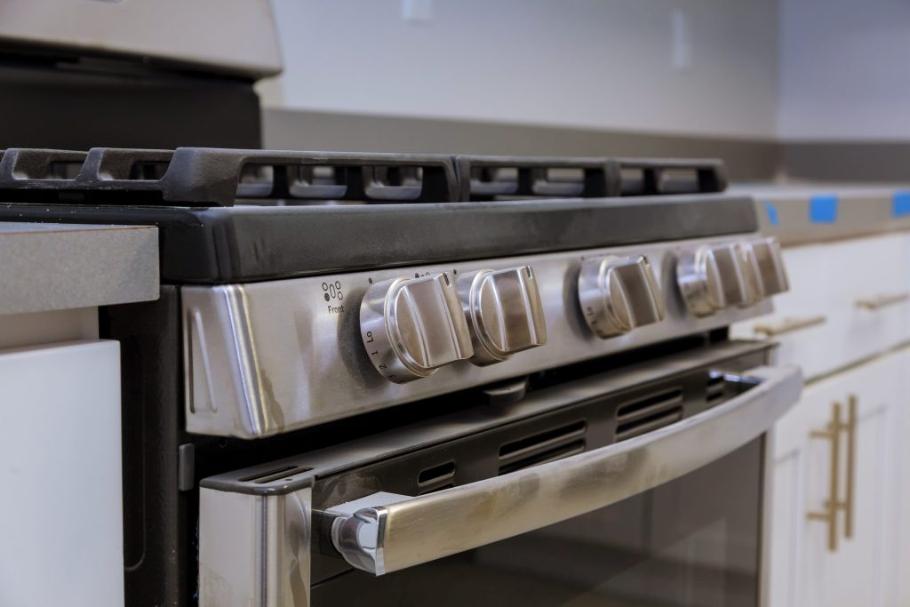A stainless range with a row of control knobs above its oven door and cast grates on top