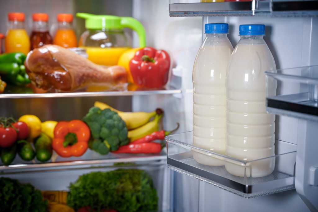 The loaded door shelf of a refrigerator standing open, milk bottles in the rack