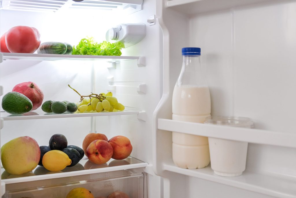 A brightly lit refrigerator interior holding fruit and a bottle of milk