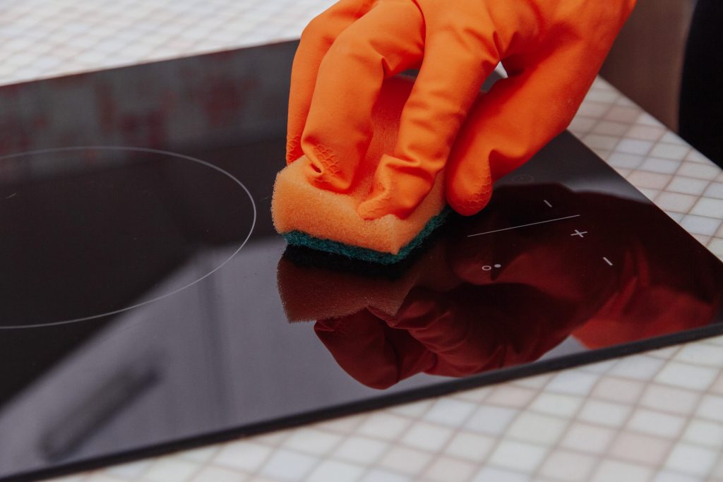 A gloved hand working across the glass surface of a ceramic cooktop