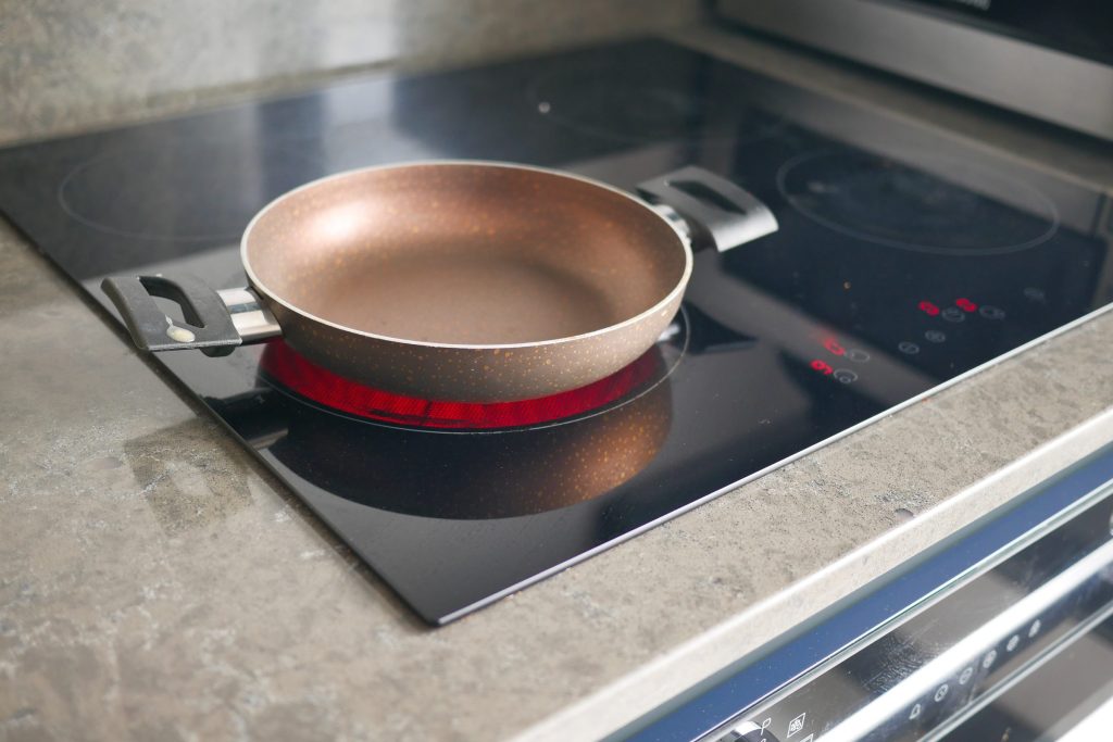 An empty pan standing on a black glass cooktop set into a stone worktop