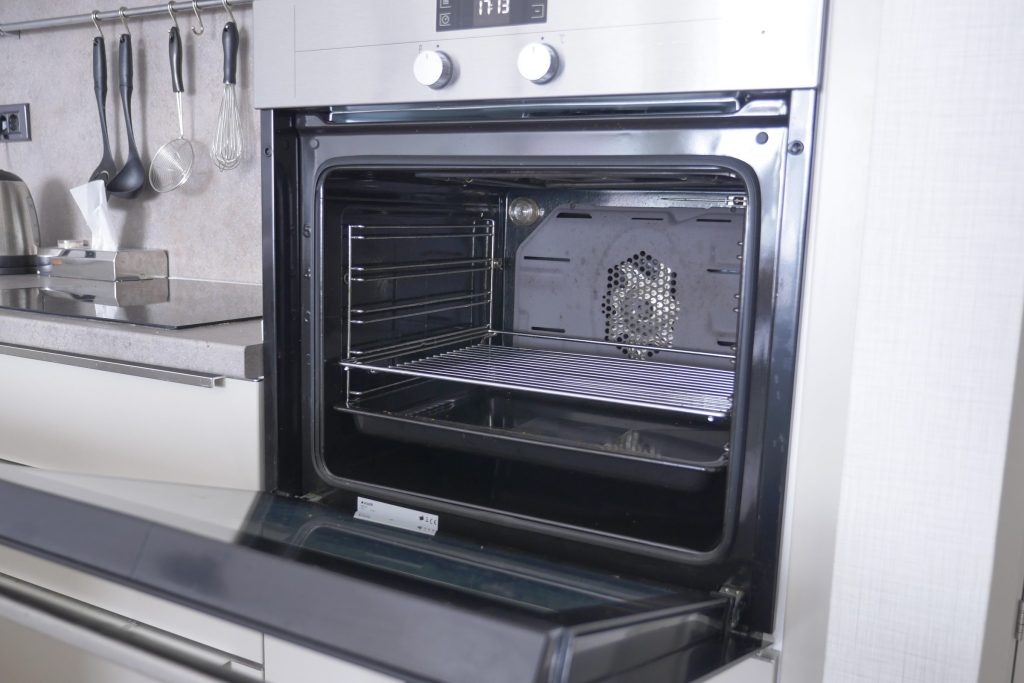 A built-in wall oven standing open on its hinges in a bright kitchen