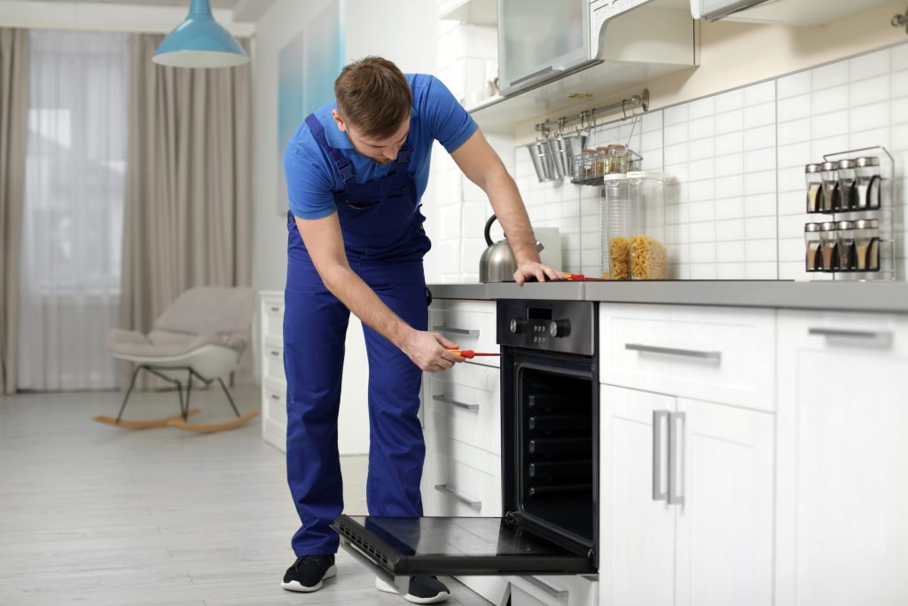 A technician with a screwdriver at the fascia of a built-in oven, its door standing open