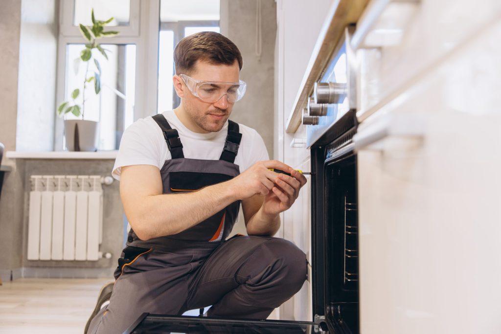 A technician in safety glasses working on the control side of a built-in oven