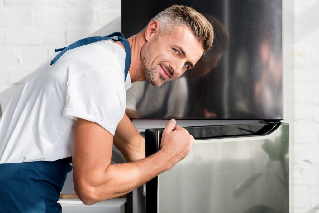 A technician opening the door of a stainless refrigerator in a bright kitchen