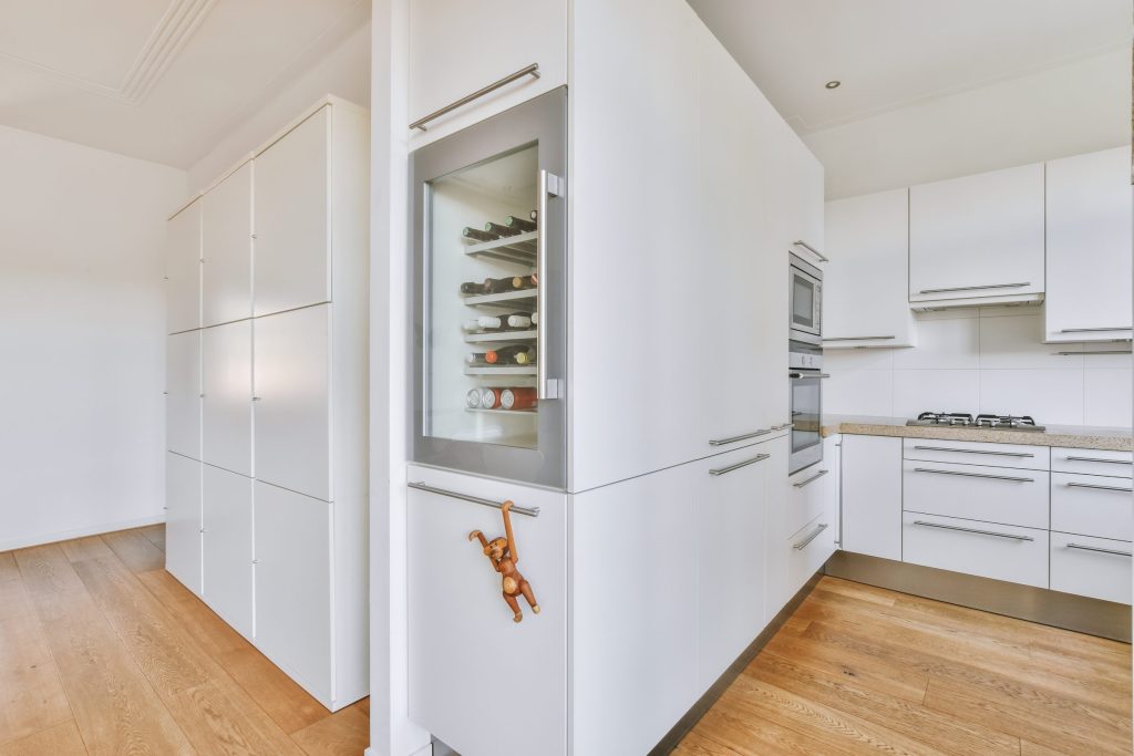 A glass-fronted wine column set flush into a white cabinetry run beside the kitchen