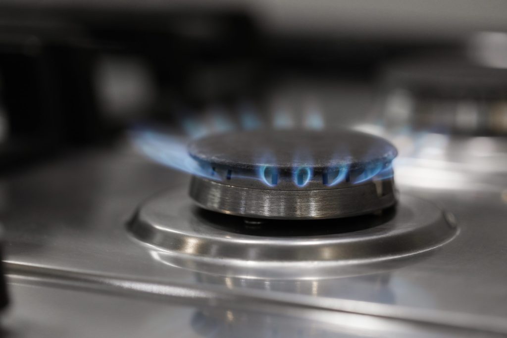 A sealed gas burner alight on a stainless cooktop, cap and ring in focus
