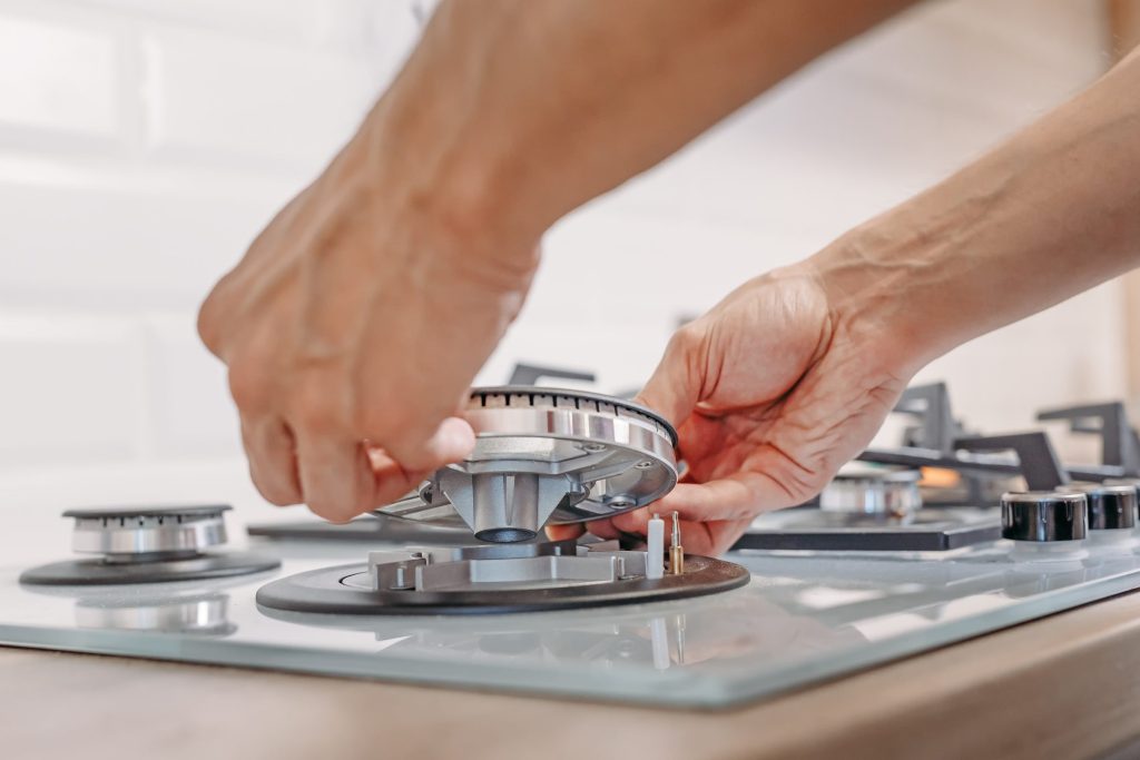 Two hands seating a burner head back onto its base on a gas cooktop