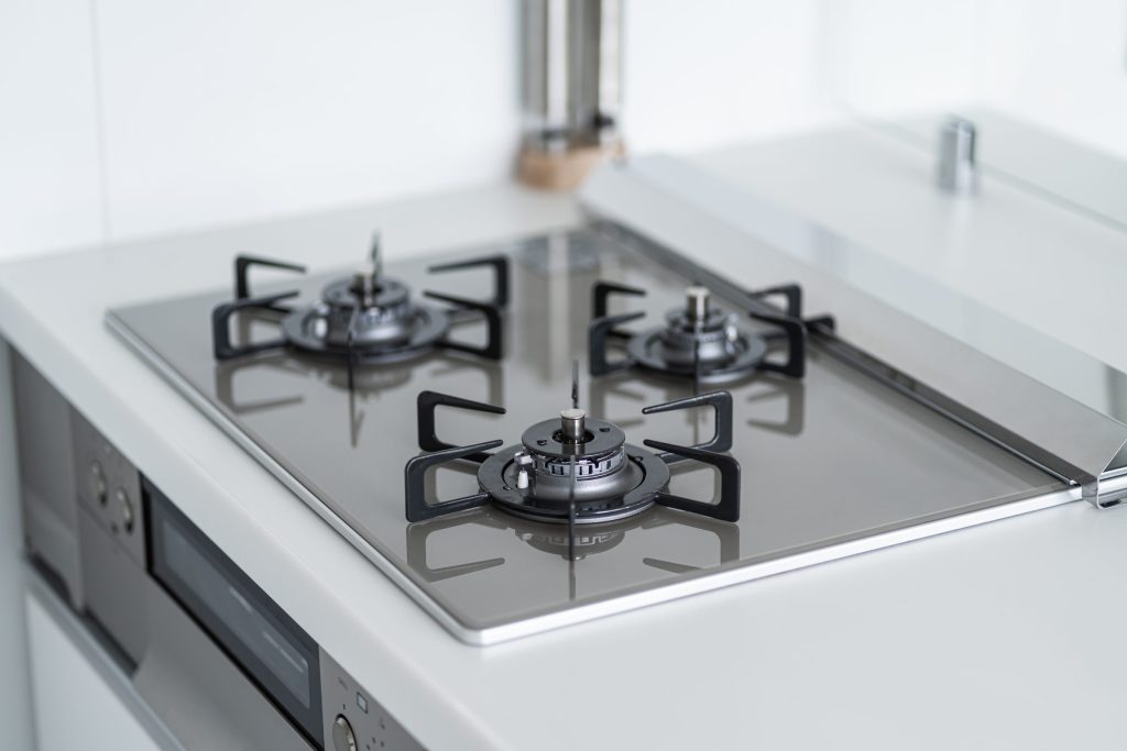 A burner head lifted clear of a white gas cooktop, igniter and grates around it