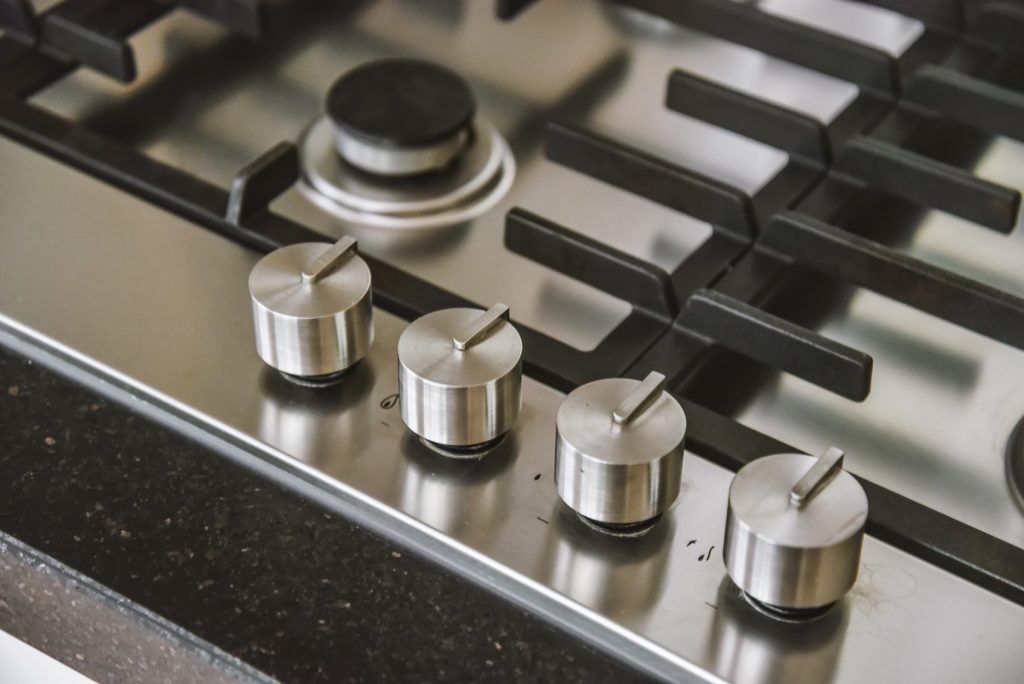 Stainless control knobs along the front edge of a gas cooktop set in dark stone