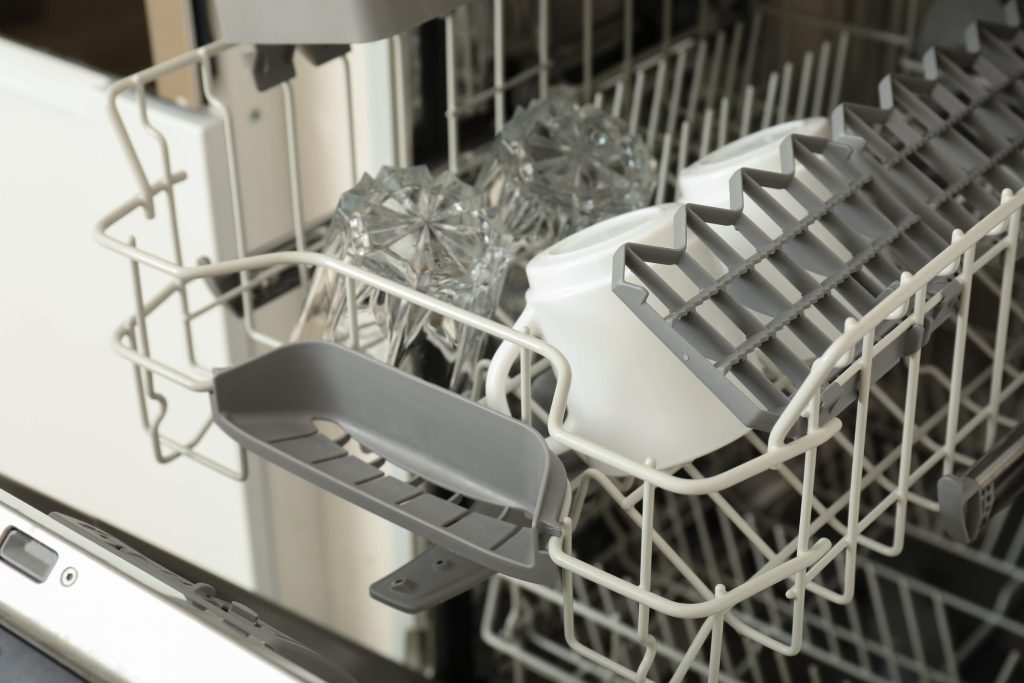 Glasses and a jug standing upturned in the upper basket of a dishwasher